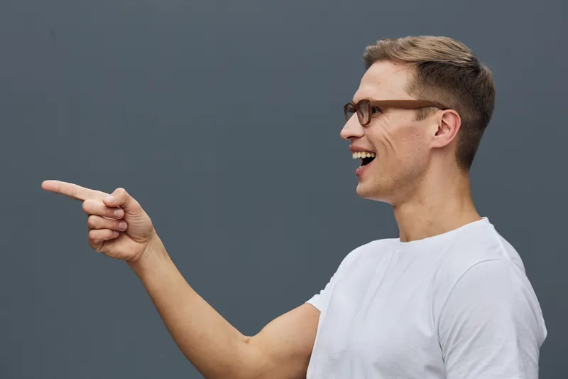 smiling caucasian man pointing finger wearing glasses white t-shirt side view digital nomad remote work technology concept
