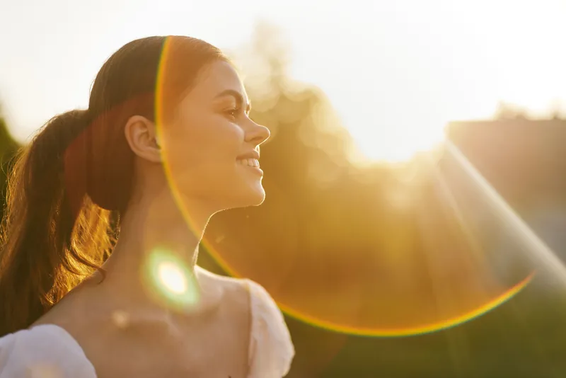 Young woman enjoying sunset outdoors, radiating joy and serenity, with warm sunlight highlighting her features and long hair
