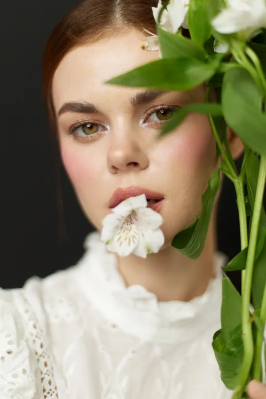Beautiful model with a flower, showcasing a fresh and natural look in a white elegant dress, capturing emotions of serenity and femininity against a dark background