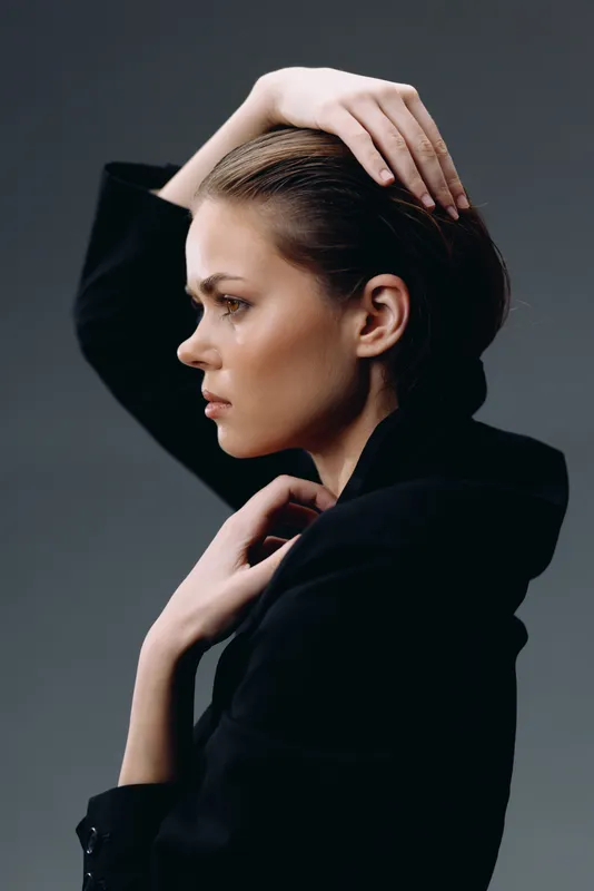 Profile of a thoughtful woman in black clothing with a serious expression and dark background