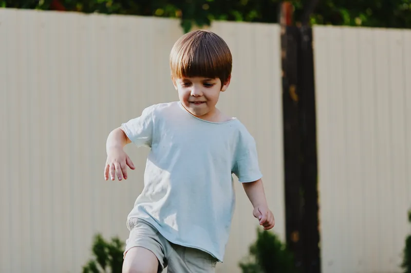 Happy boy playing outdoors, enjoying the sunshine and a carefree moment, showcasing the joy of childhood and playful spirit in a vibrant green setting.