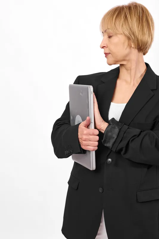 Professional elderly woman in black business suit, holding a tablet in studio with white background, side view, focused expression, modern technology communication