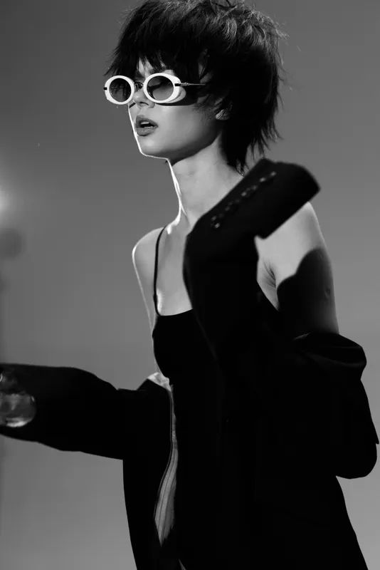 Black and white portrait of a stylish woman wearing sunglasses and modern clothing with expressive mood.