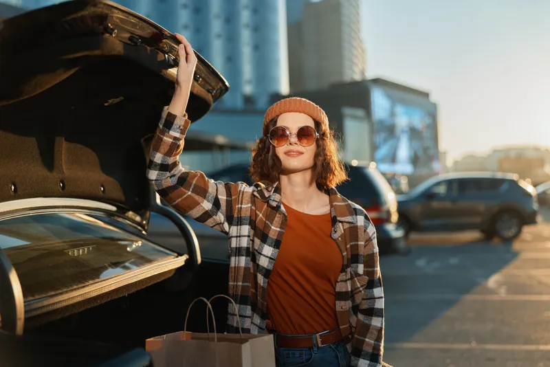 woman car shopping sunset sunglasses urban trunk smile captured in candid lifestyle scene with authenticity and golden hour glow, mindful living vibe and emotional storytelling.