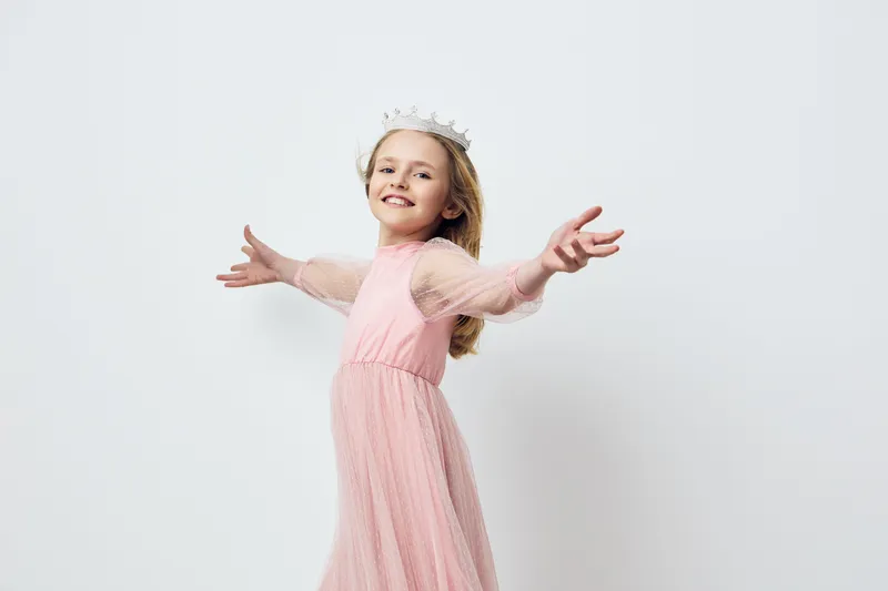 Happy girl in a pink dress with a crown, celebrating joy and innocence in a minimalist setting with a light background