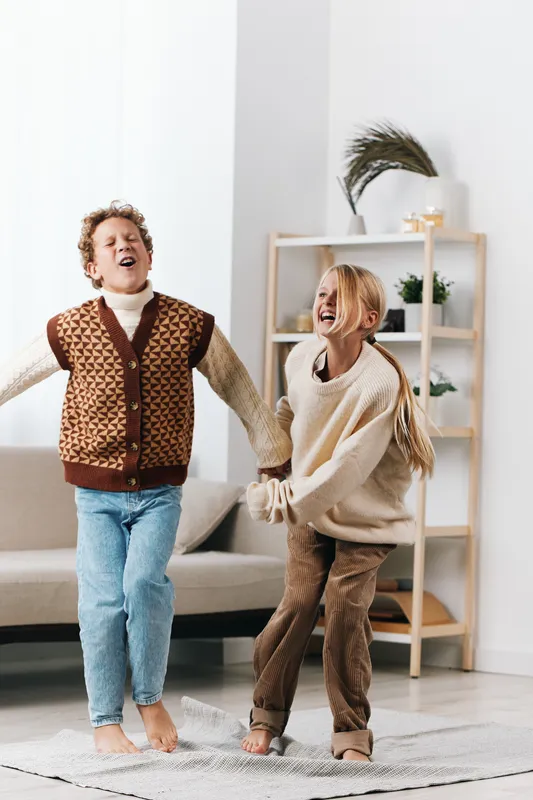 Authentic playful scene featuring children dancing indoors, cozy wardrobe, and candid movement that captures a simple school lifestyle with joy and unposed laughter.
