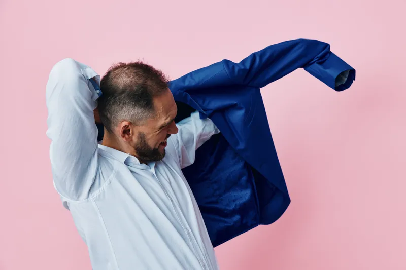 Professional man in a pastel pink studio setting, removing his blazer as he prepares for work, projecting calm confidence and focus in a vibrant color backdrop.