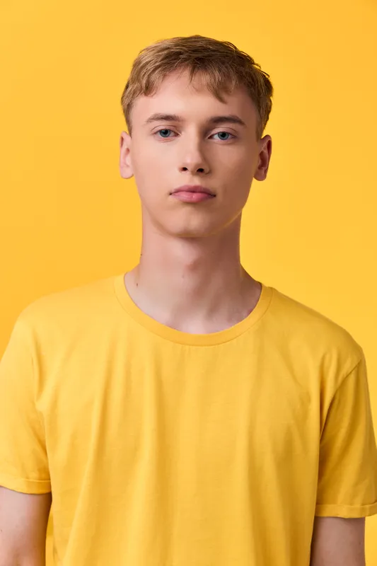 Young male model in a yellow tee against a bright yellow backdrop, a clean studio shot highlighting casual style, minimal background and relaxed expression.