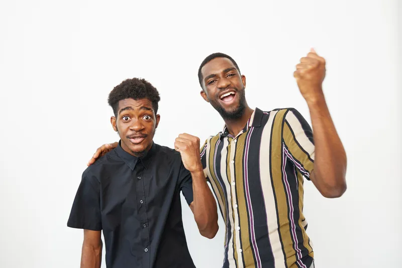 Two happy African American men celebrating together, showing excitement and joy. Their vibrant outfits and cheerful expressions convey a sense of camaraderie and positivity.