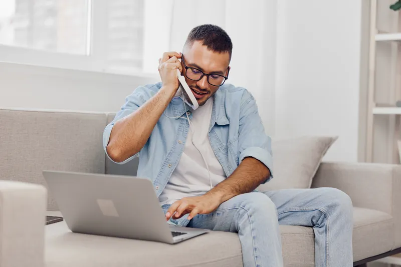 Motivated man engaging in a phone call while working on a laptop, representing the blur between personal and work life amid modern digital distractions.
