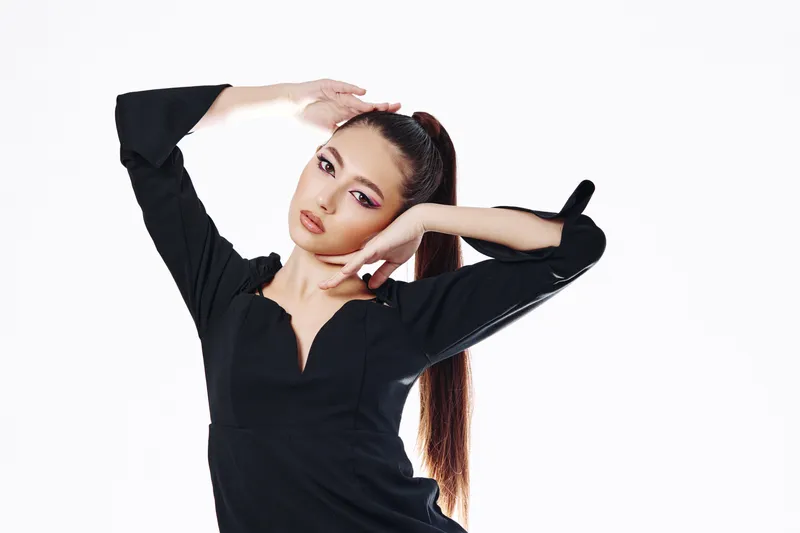 Fashion model with dramatic makeup poses gracefully in an elegant black top against a white background. Concepts include beauty, fashion, creative expression, and modern style.