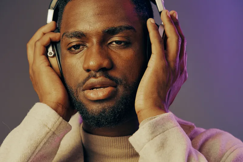 A young man enjoying music with headphones, displaying a serene expression in a softly lit, colorful background Perfect for music and relaxation themes