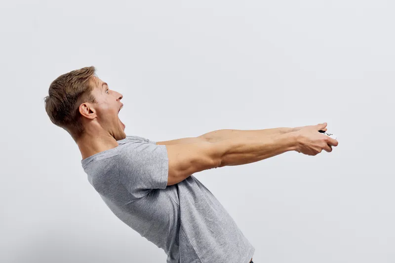 Young man stretching out his arms in a dynamic pose, wearing casual gray t-shirt. Expressing freedom, energy, and vitality in a bright studio setting with a plain background. Lifestyle concept, fitnes