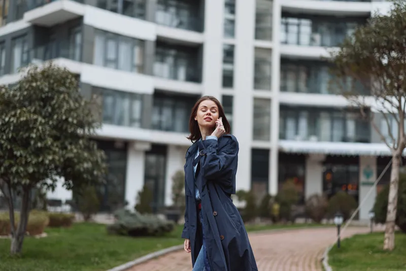 Young woman walking outdoors in urban environment wearing long dark coat, casual style, relaxed expression, modern city background, daytime scene