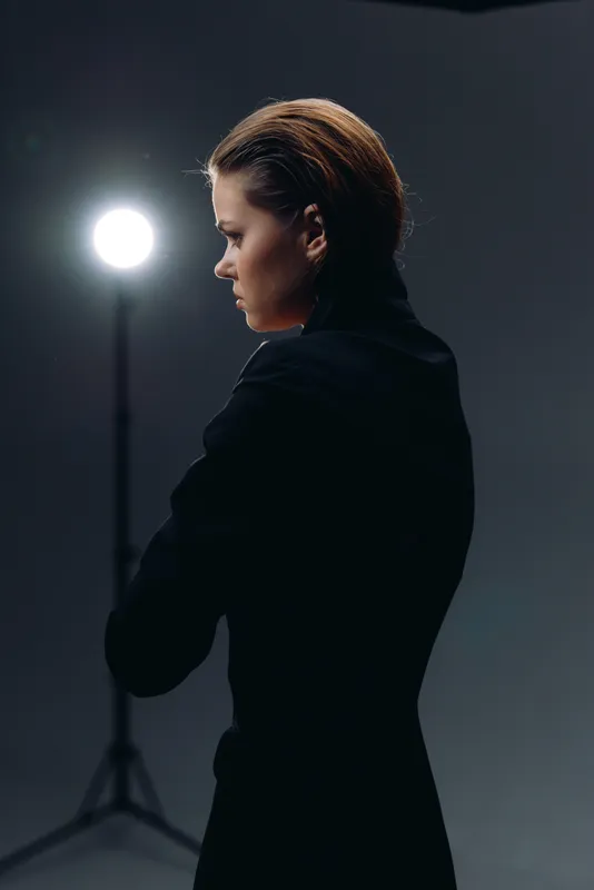 Profile of a serious woman in black with short hair against dark background and bright studio light