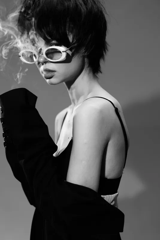 Black and white portrait of a stylish woman wearing sunglasses and smoking with an edgy, modern look
