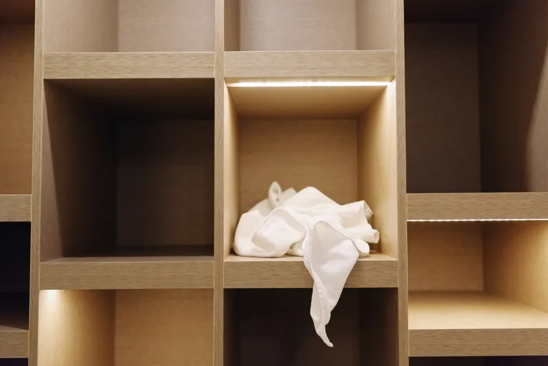 Wooden cubbies and shelves glow with warm light, a crumpled white cloth resting in a empty compartment, showcasing organized storage space and minimalist modular cabinetry in a calm interior.