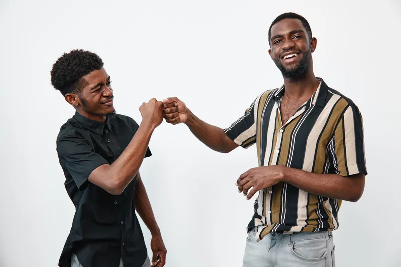 Two young black men with dark skin fist bumping and smiling in casual clothes on white background. Friendship, happiness and positive connection between african american friends.