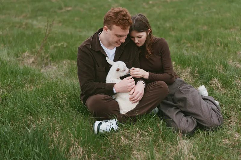 Cozy couple enjoys a sunny day on the grass, cuddling a fluffy white dog, sharing smiles and gentle moments in a peaceful park setting, casual outfits, warm light, affection and companionship.