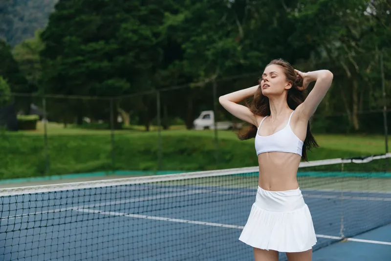Female tennis player celebrating victory outdoors in a white athletic outfit, demonstrating confidence and joy on a sunny day