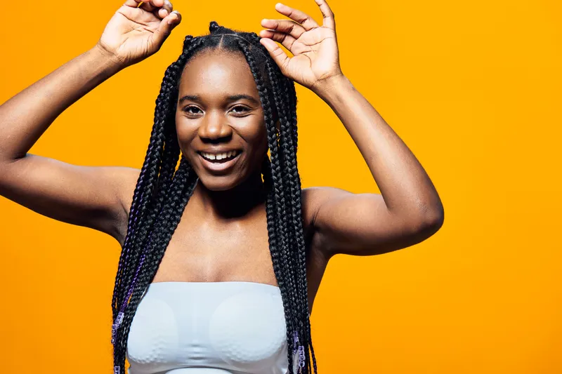Young woman with braided hair smiling against a vibrant orange background, embodying joy and celebration with energetic poses and a playful expression