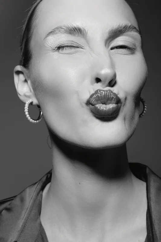 Close-up portrait of a young white woman with fair skin winking and puckering lips. Studio shot in black and white focusing on facial expression and beauty concept.