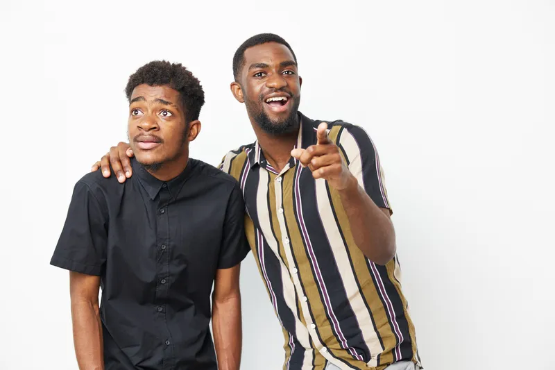Two African American men smiling and having fun together, showcasing friendship and joy in a vibrant and playful atmosphere with a bright background.