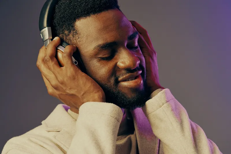 A joyful young African man enjoying music with headphones, smiling softly against a colorful gradient background, capturing the essence of relaxation and happiness