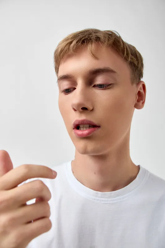 Closeup of a youth male in a white tee examining his fingers with a thoughtful expression, calm lighting, subtle texture and focus on the hand