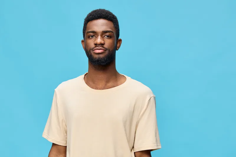 Young African man in beige t shirt against a vibrant blue background, exuding confidence and calmness, perfect for lifestyle and fashion concepts