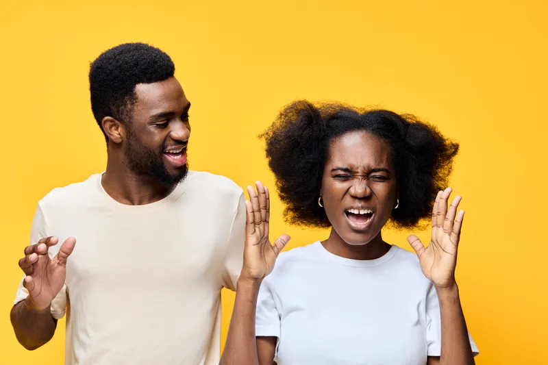 Joyful young African couple having fun together on a vibrant yellow background, showcasing playful emotions and vibrant energy while dressed casually in light clothing