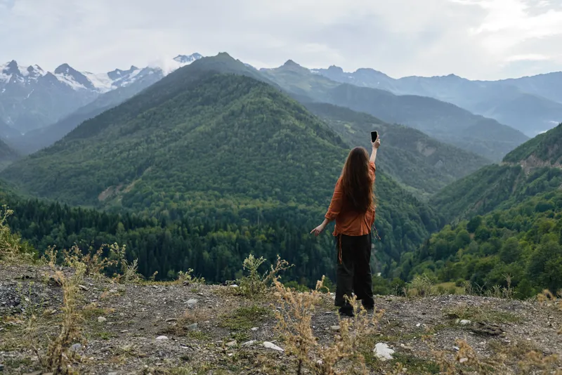 Woman stands on a rocky overlook in the outdoors, gazing at a vast mountain range and distant horizon, capturing a moment of adventure and awe.