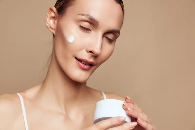 Calm portrait of a woman with closed eyes applying cream, gentle skincare moment, soft lighting, natural colors, smooth skin, minimal makeup, everyday beauty