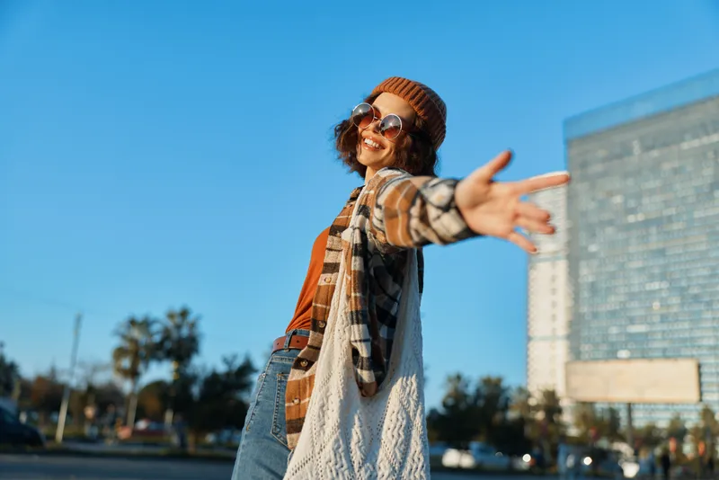 Woman smiling in urban street with arms outstretched, joyful candid moment in warm sunlight, authenticity and candid lifestyle captured with golden hour glow and mindful living vibe.