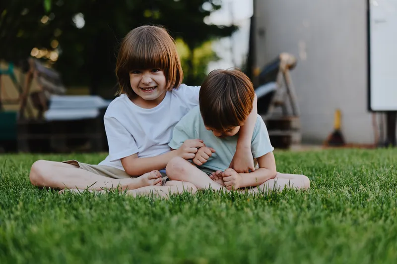 Joyful children playing together on the grass, showcasing a moment of sibling bonding and happiness in a sunny outdoor setting.