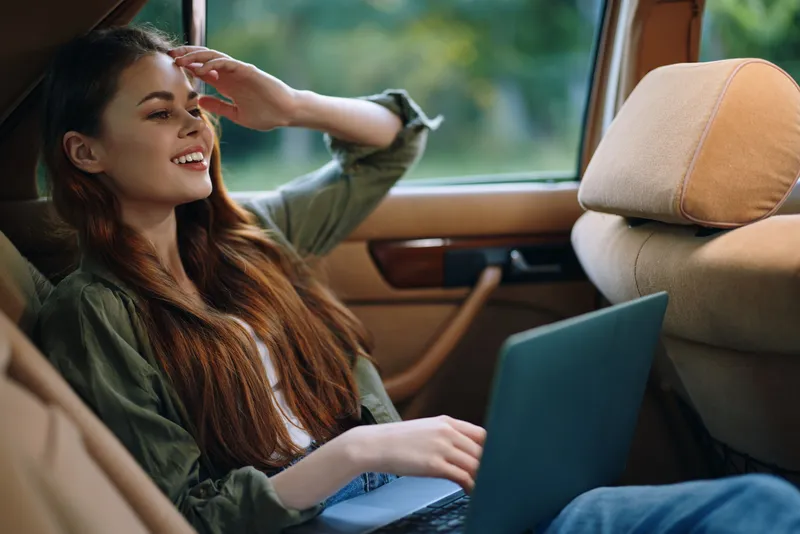Young woman working on a laptop in a car, showcasing creativity and relaxation in a nature-filled setting, highlighting the concept of remote work.