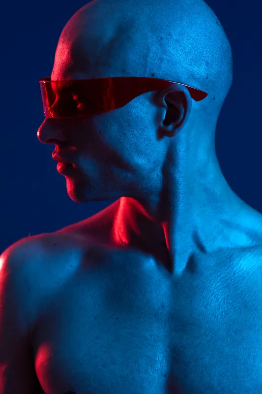 Stylish man in vibrant red sunglasses poses against a contrasting blue and red background, showcasing a modern, artistic vibe. Perfect for creative projects.
