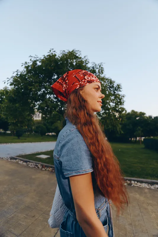 Lifestyle woman wearing modern boho-western denim street style with long red hair and a red bandana outdoors, captured in warm film color tones.