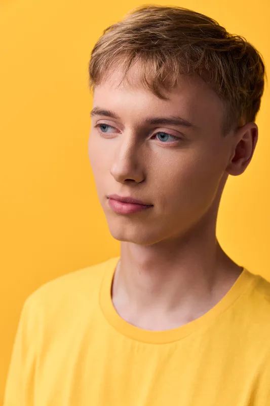 young man in yellow shirt with yellow background, minimal style, calm mood, fashion and lifestyle aesthetics, suitable for wellness themed campaigns and contemporary editorial visuals