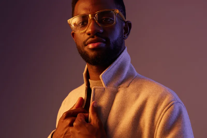 Stylish African American man in a light sweater, posing confidently with an elegant expression and warm lighting, ideal for fashion and lifestyle concepts