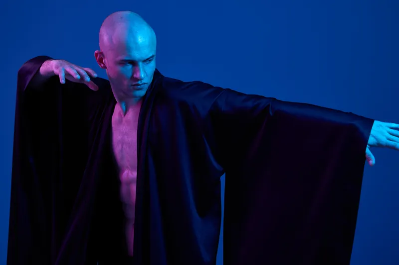 Proud man in flowing black robes, showcasing elegance and creativity in a vibrant blue light setting. A mesmerizing display of artistry and movement.