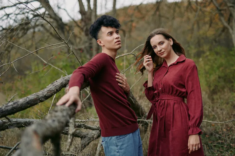 A candid duo stands in an autumn woodland, wearing matching burgundy outfits, conveying authenticity and credibility through a natural pose and calm, sincere expressions.