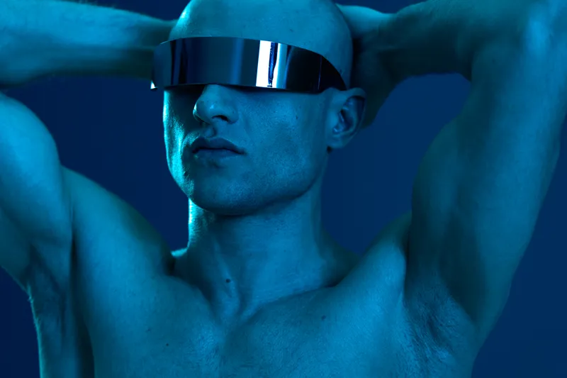 Stylish man with futuristic sunglasses posing confidently against a vibrant blue backdrop, showcasing a modern and edgy aesthetic. Ideal for fashion and technology themes.