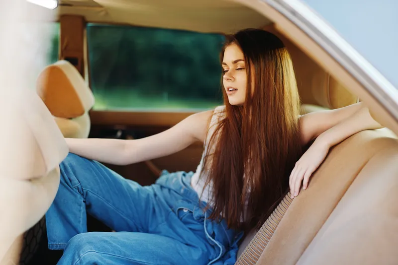 Young woman in casual attire relaxing in a vintage car, expressing a serene vibe with long hair and denim outfits, perfect for lifestyle and fashion concepts.