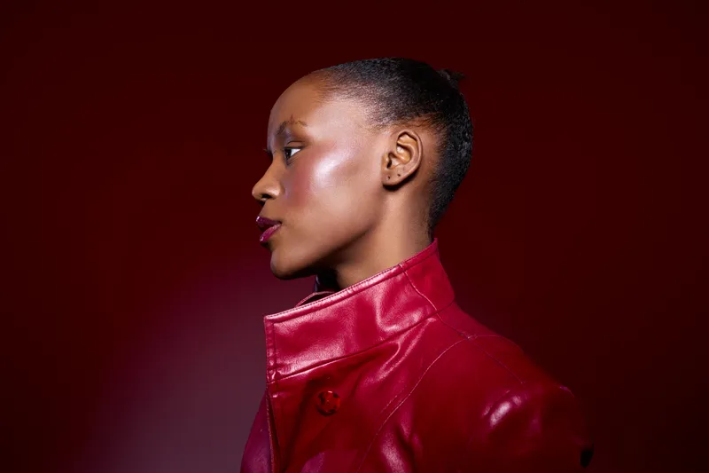Profile of an African American woman with dark skin wearing a red leather jacket against a dark red background. Concept of fashion, beauty, confidence, and style in studio lighting.