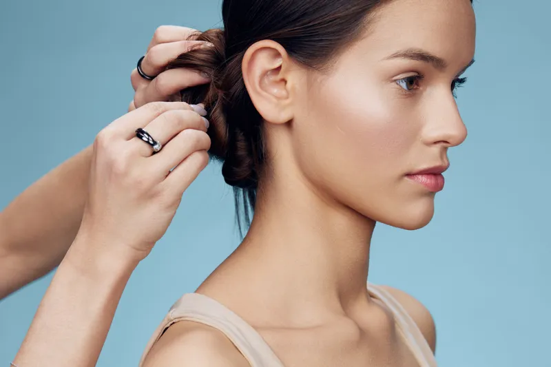 Female model with a sleek hairstyle being styled, showcasing a serene expression against a soft blue backdrop and minimalistic fashion