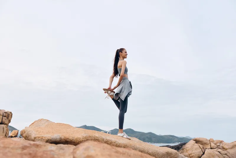 Young woman practicing yoga on rocky terrain, showcasing strength and flexibility in sporty attire, embodying a healthy lifestyle and tranquility