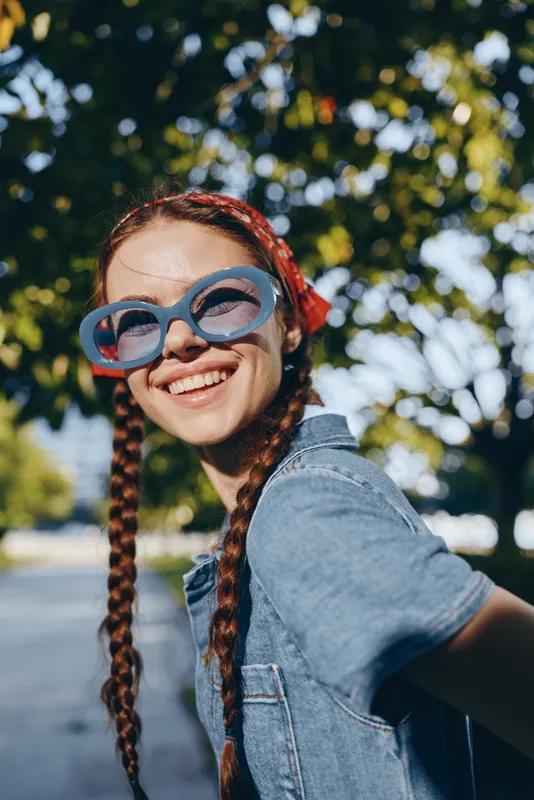 Lifestyle woman wearing modern boho-western denim street style outfit with film color effect smiling outdoors under bright sunlight on a summer day.