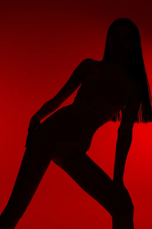 Silhouette of a fit woman sport fitness model posing against a vibrant red background, showcasing strong body posture and athletic form with dramatic lighting.