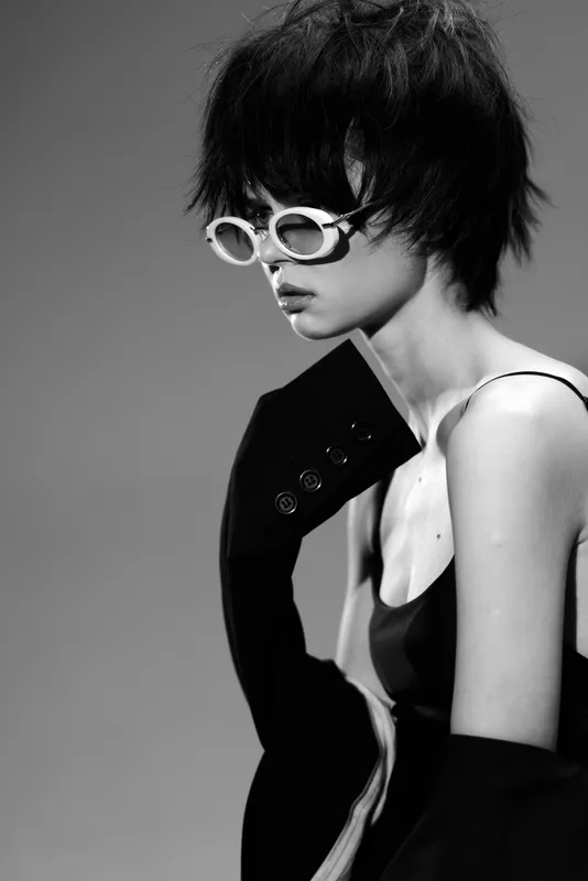 Black and white portrait of stylish woman wearing sunglasses and a blazer with modern haircut.